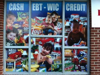 Convenience store front with window signage reading in all caps: "CASH EBT WIC CREDIT." Pictured below is a collage of smiling babies and ultra-processed junk foods including chips and sodas.