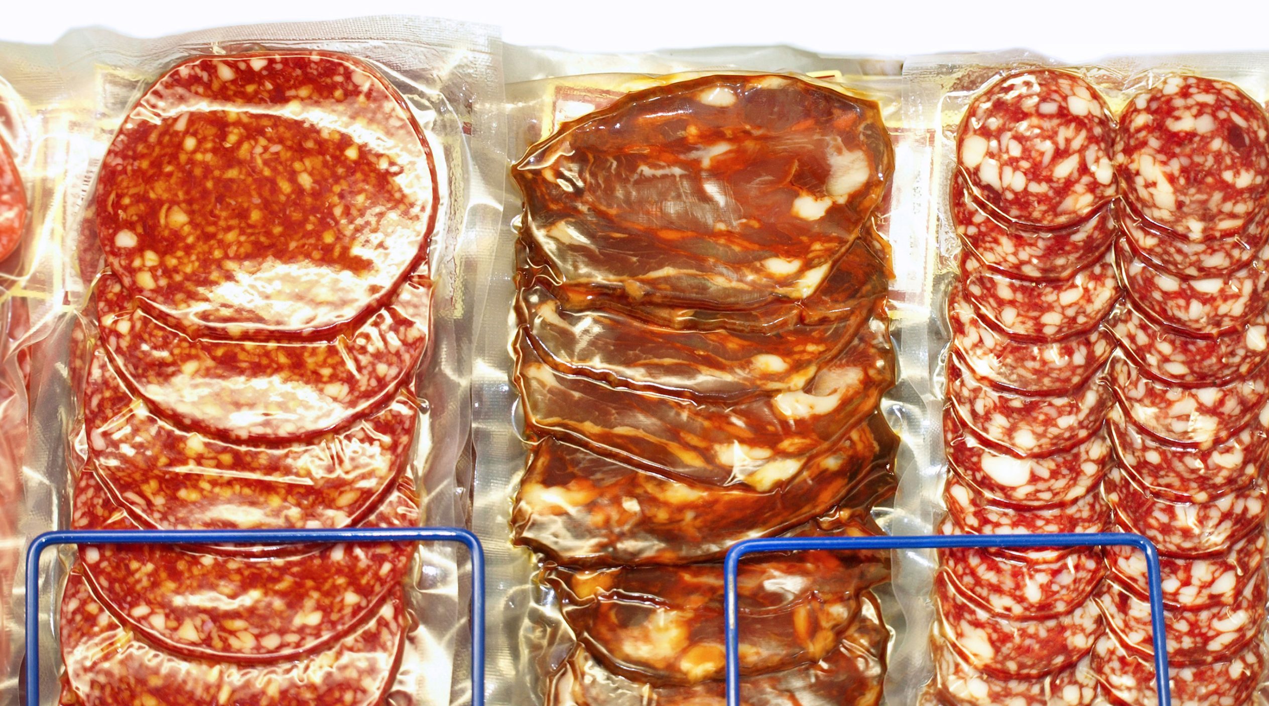 Vacuum-sealed, sliced red processed meat in a store shelf