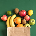 brown grocery bag with fruit spilling out on green background