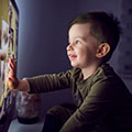 Small child sitting in front of a bright TV, smiling and touching the screen